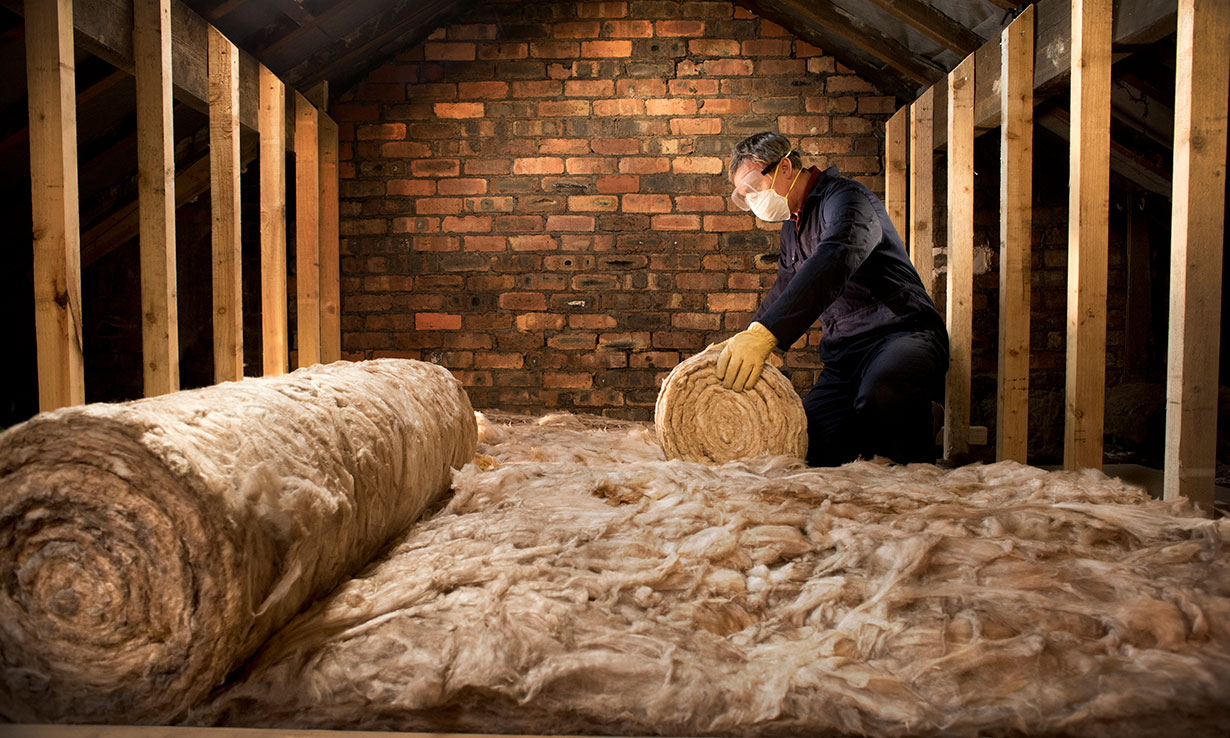Man fitting loft insulation in roof space